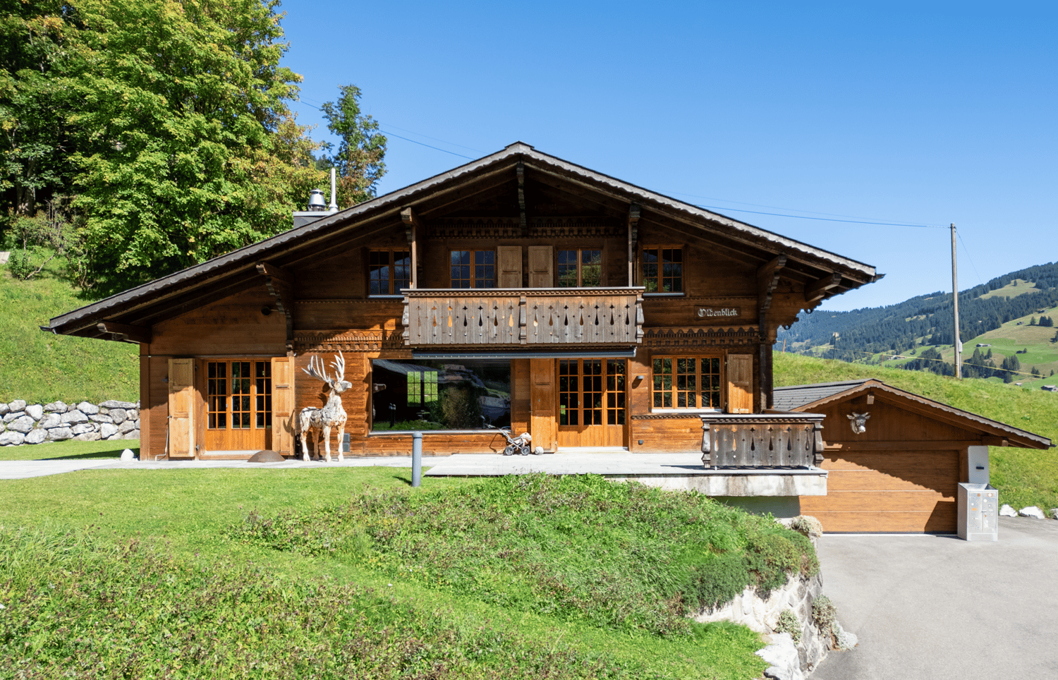 wooden chalet, gable roof, balcony, deer statue, stone wall, garage