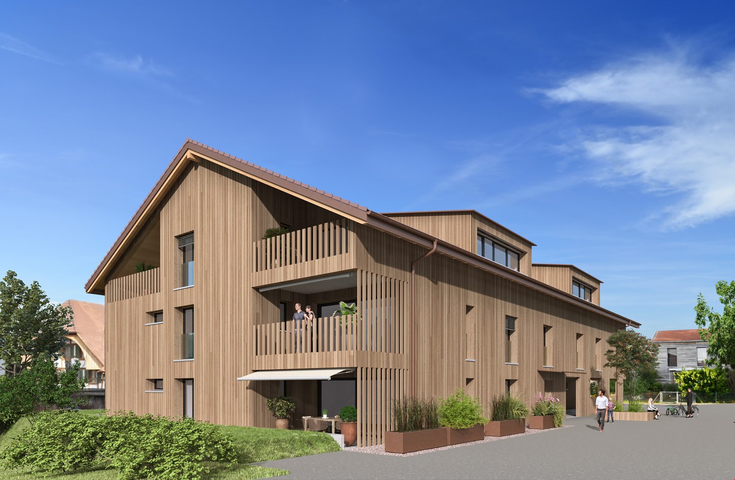 3-story wooden building with a slanted roof, balconies, and large windows. The building has a modern, eco-friendly design with a natural wood exterior. There are people visible on the balconies and a paved walkway in front of the building.
