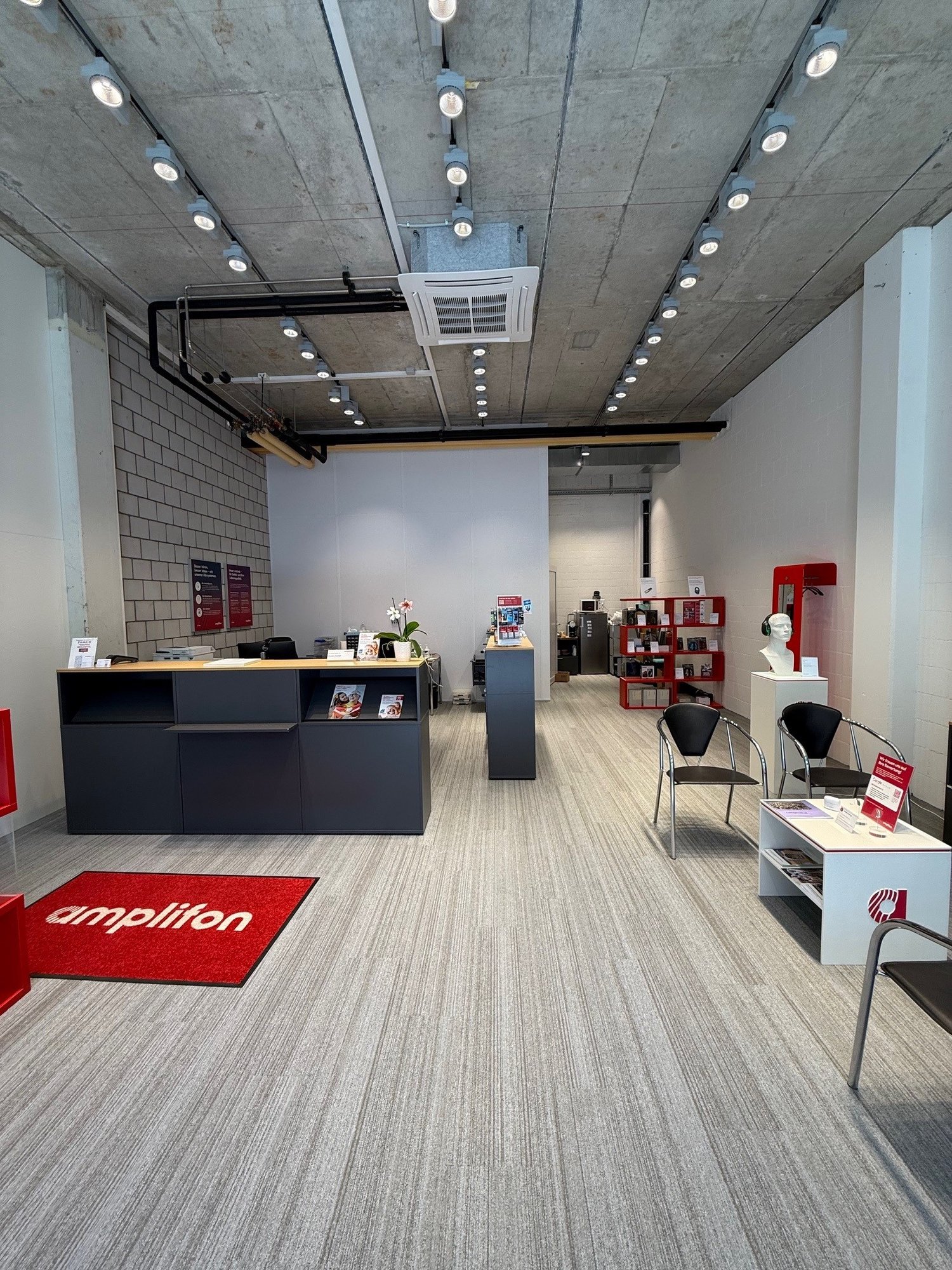 Interior of an office with a grey and white color scheme, carpeted floor, multiple modern fixtures, reception desks, chairs, tables, and decorative items