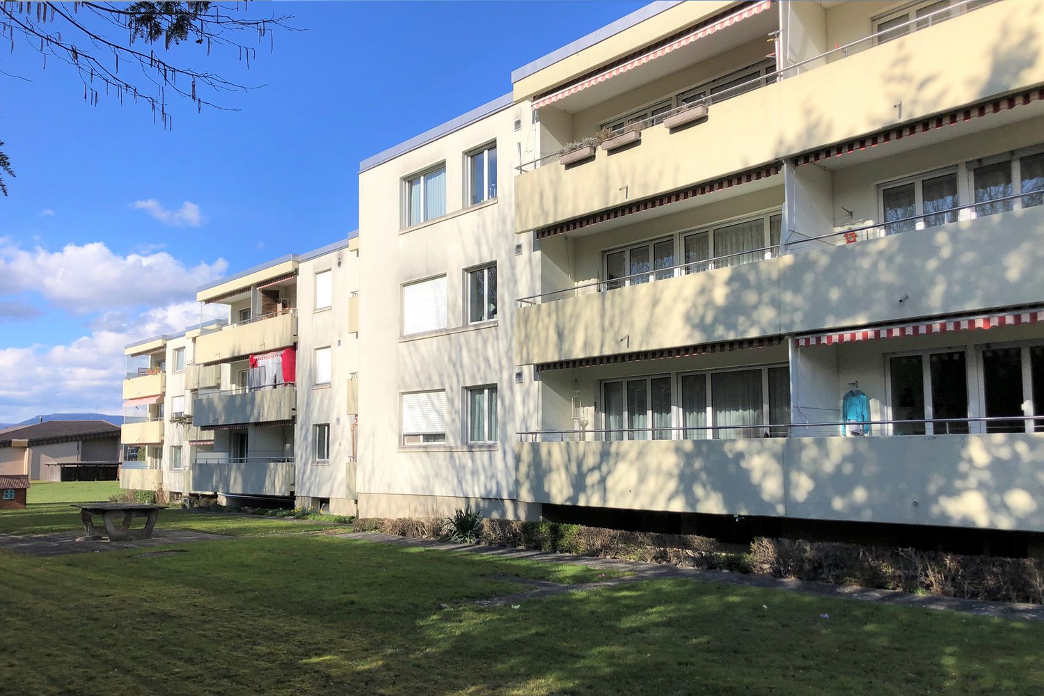 4 story apartment building, each floor has balcony, garden in front