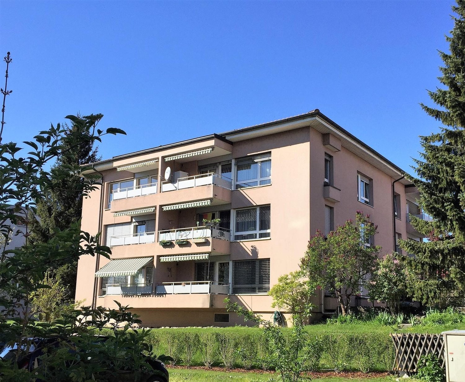 multi story residential building with 4 floors, beige colored exterior, small shrubs and plants, some balconies visible