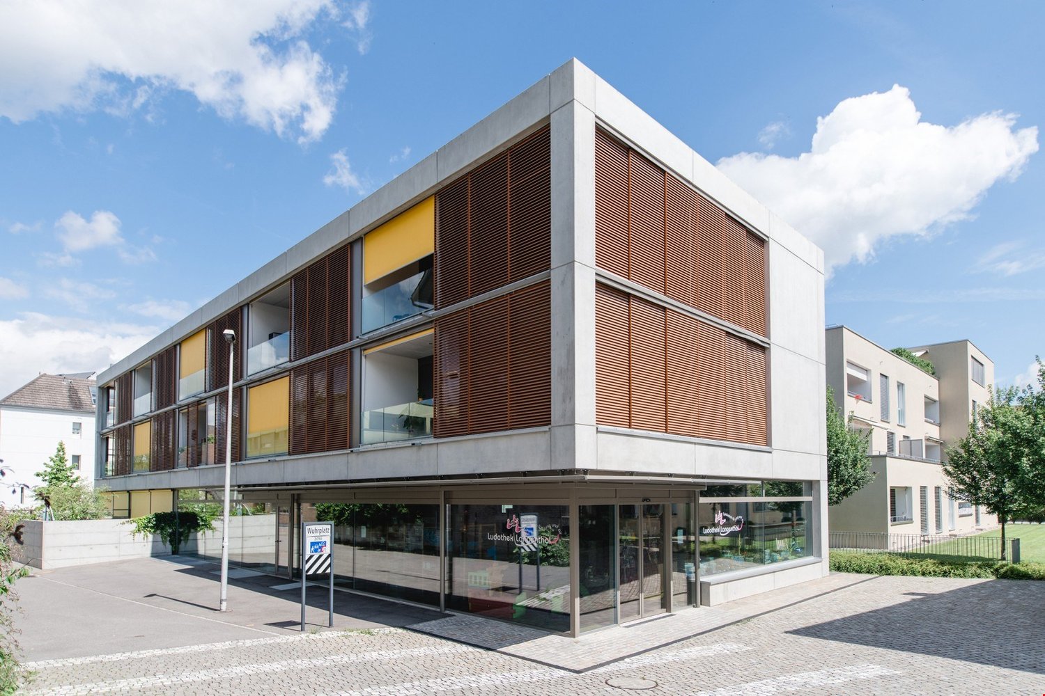 modern building, concrete, glass windows, storefront, parking area, surrounded by greenery
