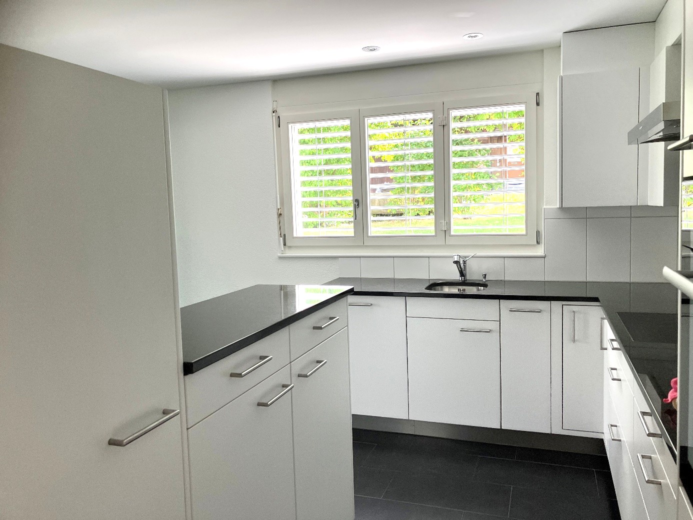 modern kitchen with white cabinets, black countertop, stainless steel sink, and a window with blinds
