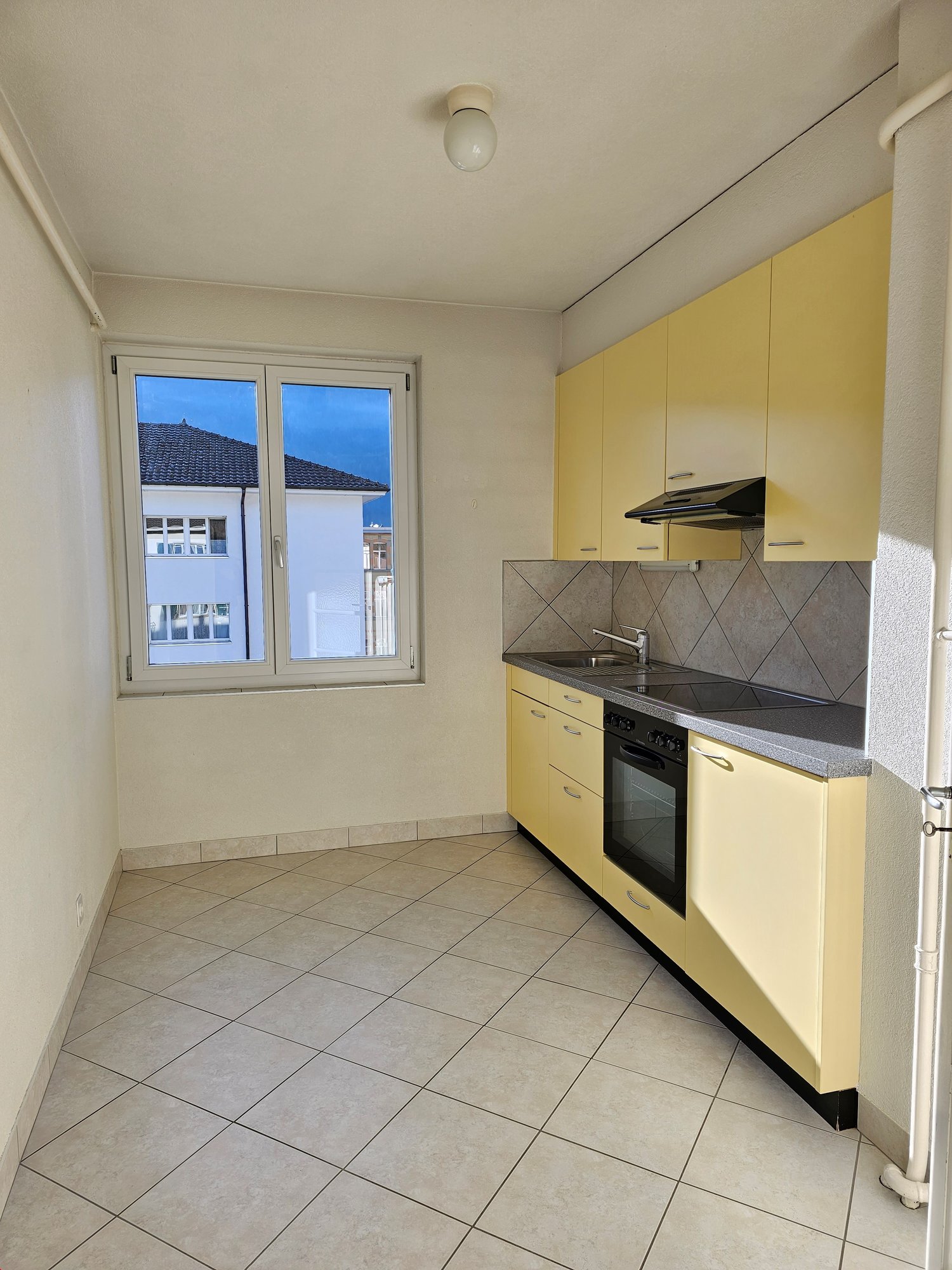 Spacious kitchen with yellow cabinets, tiled floor, and a window overlooking the exterior. The kitchen is equipped with a stove, oven, and a dishwasher.