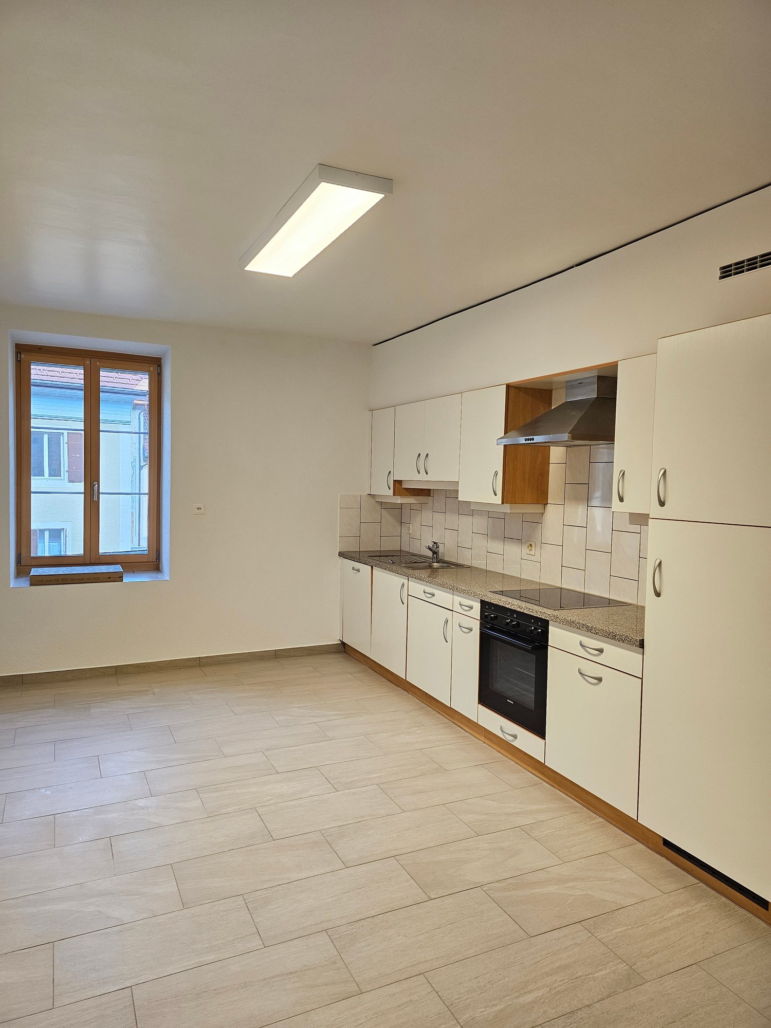 Modern, clean kitchen with white cabinetry, a tile backsplash, wooden flooring, and stainless steel appliances.