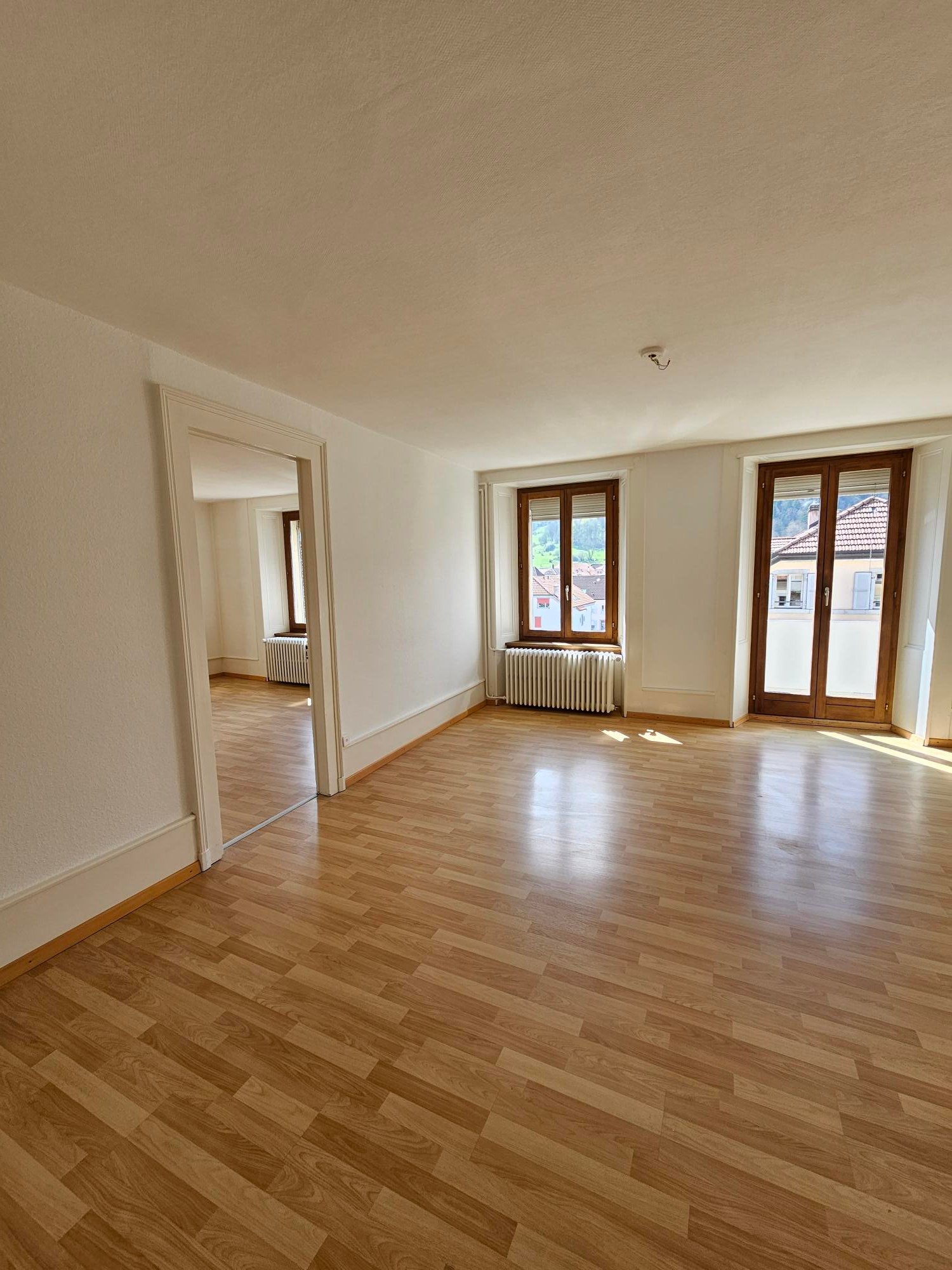 empty room, wooden floor, white walls, two windows, sliding doors, radiator