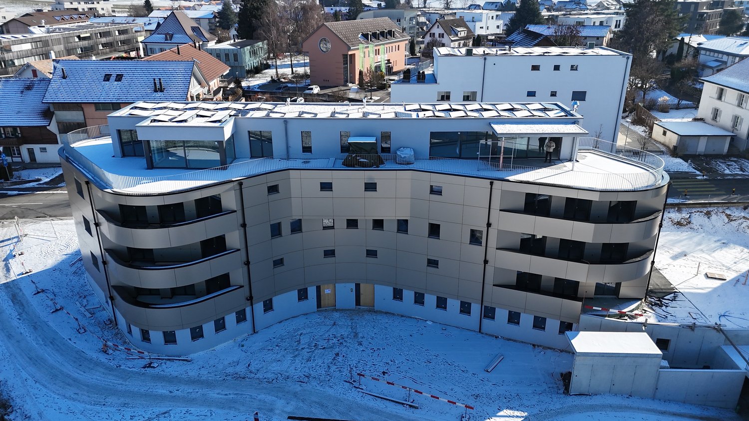 Curved, multistory building, with multiple balconies, large windows, and rooftop solar panels