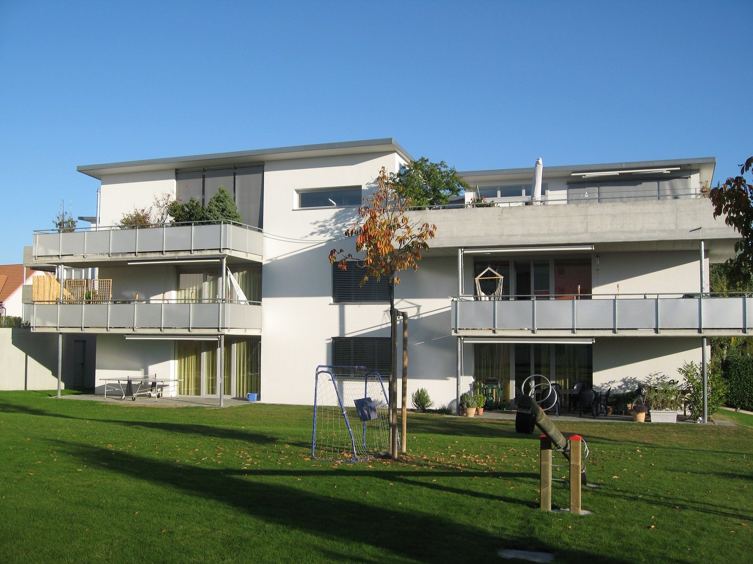 White two-story house, two balconies, green lawn, play equipment