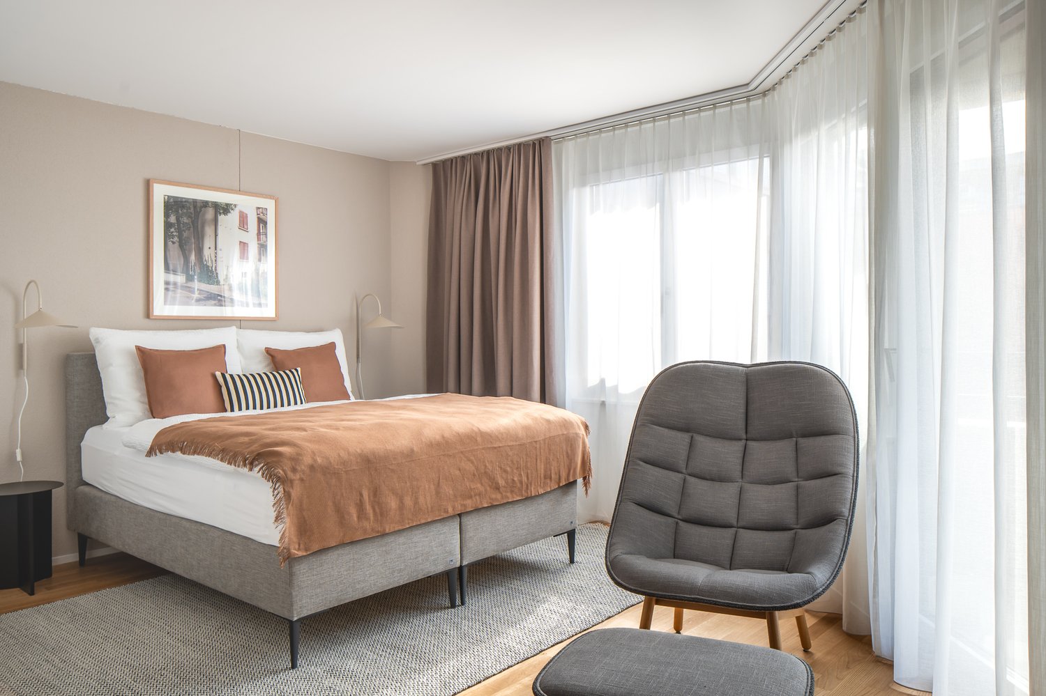 bedroom with bed, bedside tables, picture frame, curtains, chair, ottoman, carpet