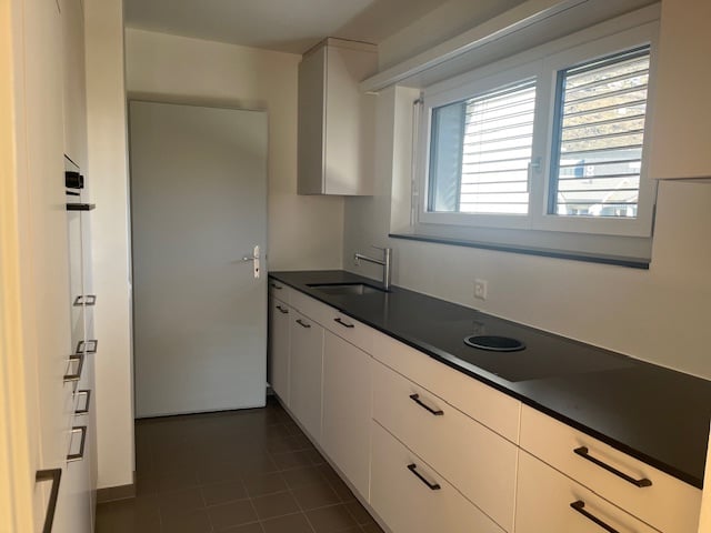 modern kitchen, stainless steel sink, black countertop, white cabinets, window with blinds, white appliances