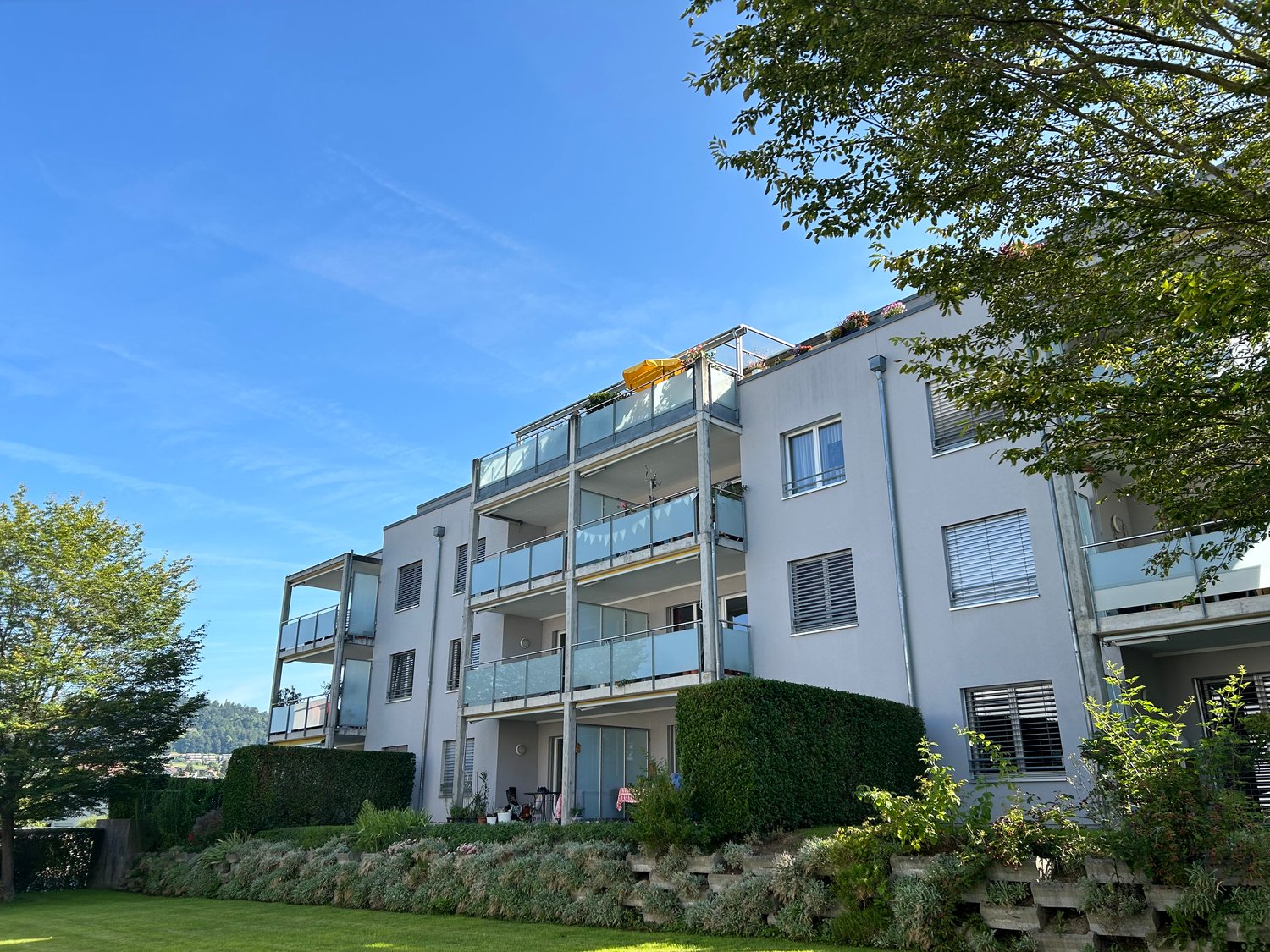 white apartment building, multiple balconies, green plants and trees in the surroundings