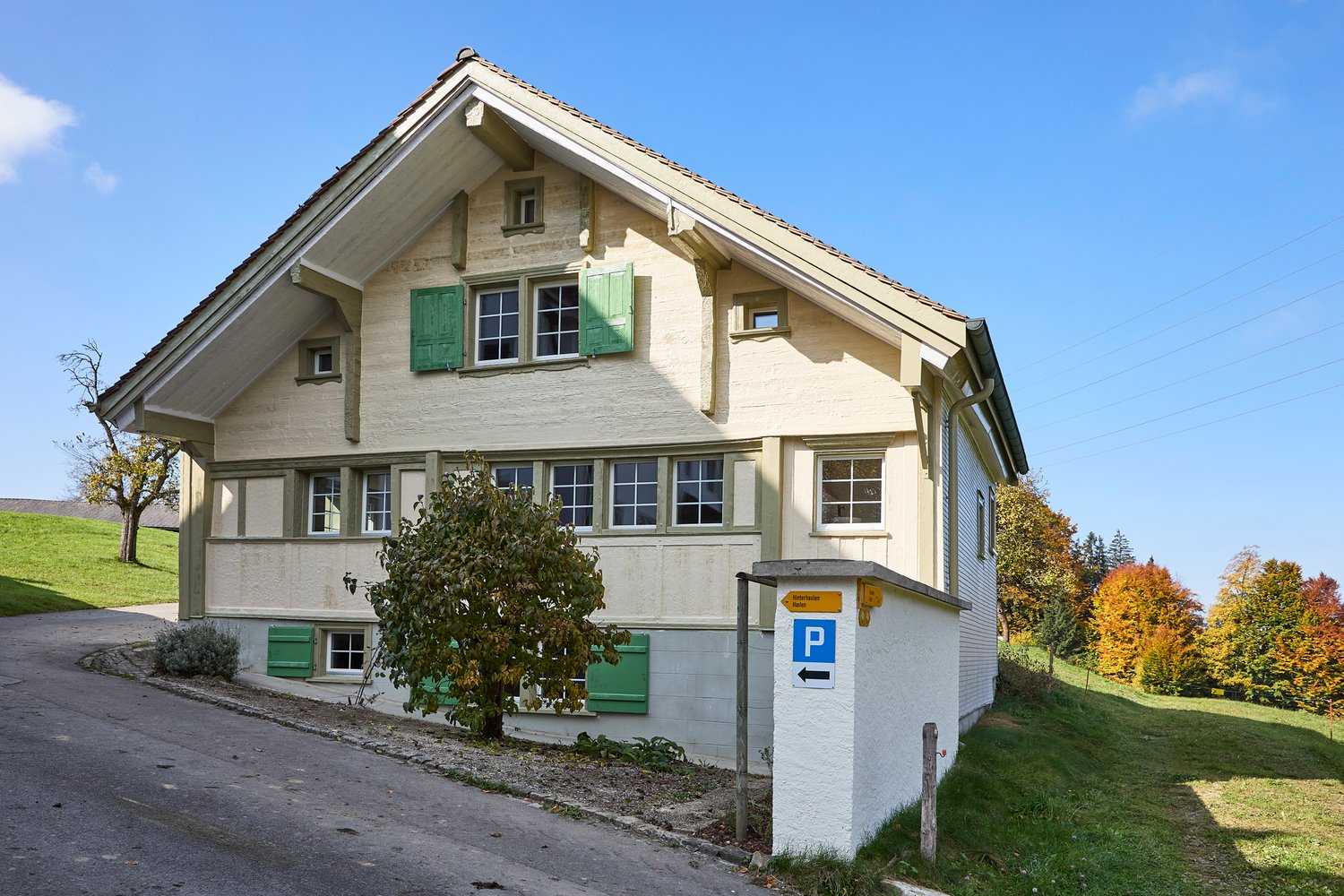 Two-story house, light beige walls, green shutters, small garden in front