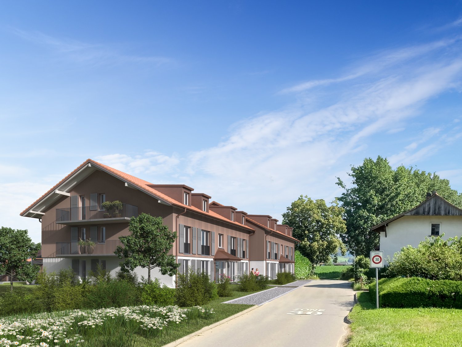 A multi-story apartment building with brown siding and red tile roofs. The building has balconies on each floor and is surrounded by trees and greenery. There is a paved walkway leading to the building.