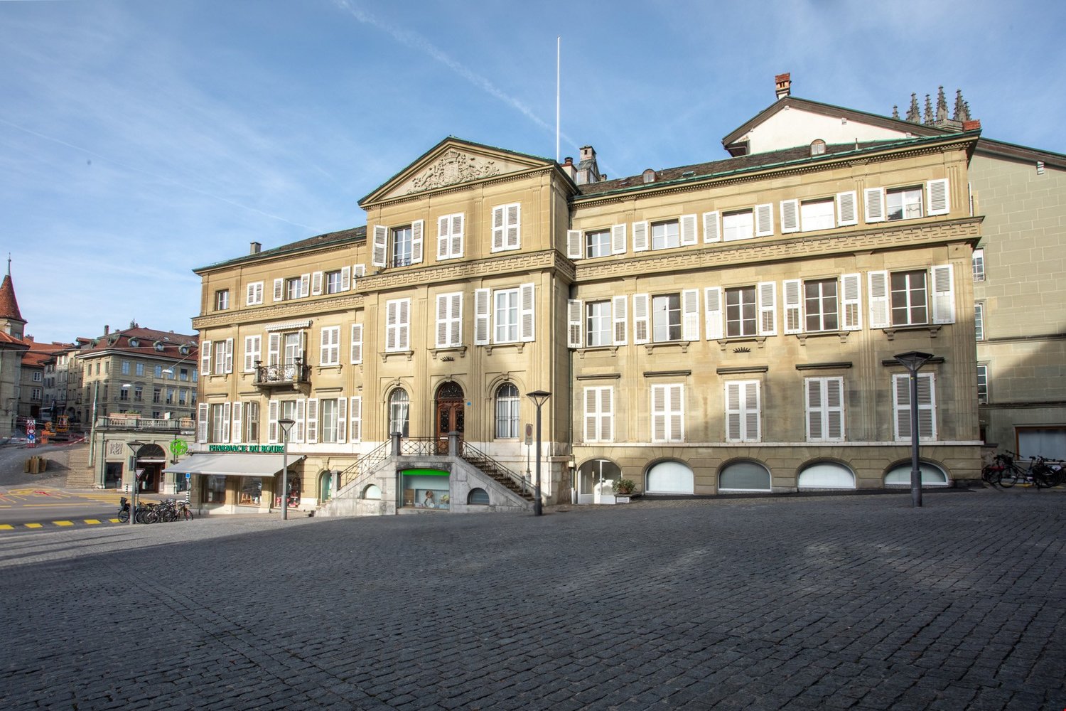 2 story building, beige color, multiple windows, large entrance with staircases, pavement