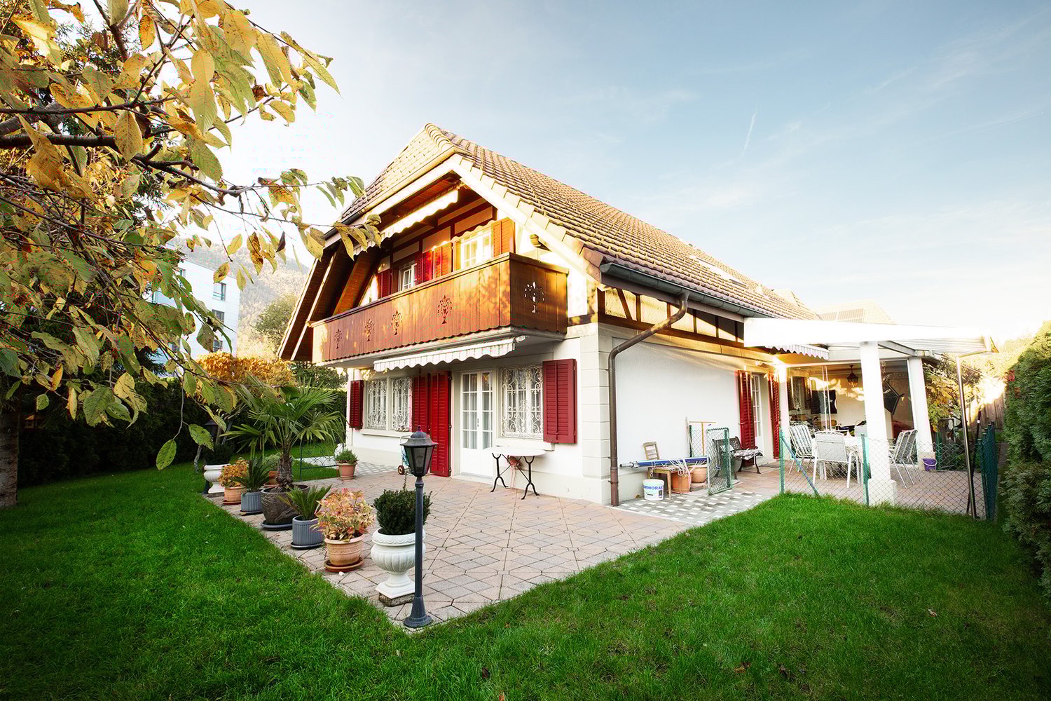 House with balcony, wooden trim, white exterior, tiled patio, grassy yard, patio furniture, potted plants
