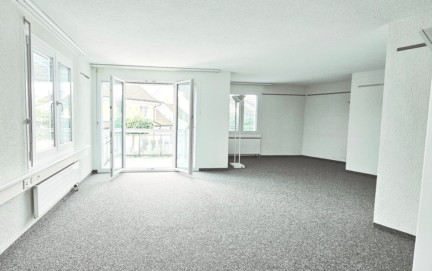 An empty room with a balcony and sliding glass doors leading to it, white walls, and a carpeted floor.