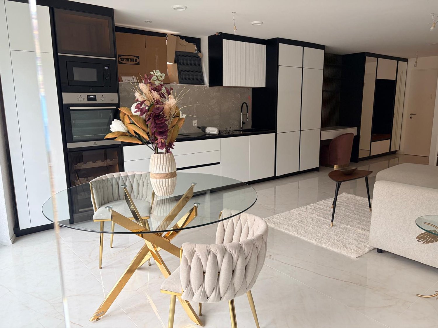 glass table, chairs, couch, cabinet, carpet, countertop, oven, microwave, sink, faucet, flower vase