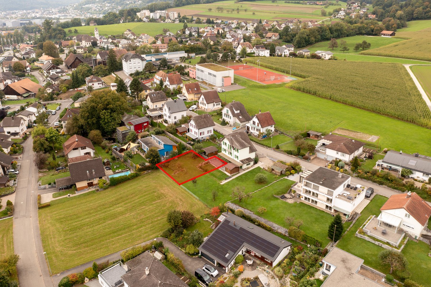 aerial view of a residential area, with various houses, solar panels, and a tennis court.