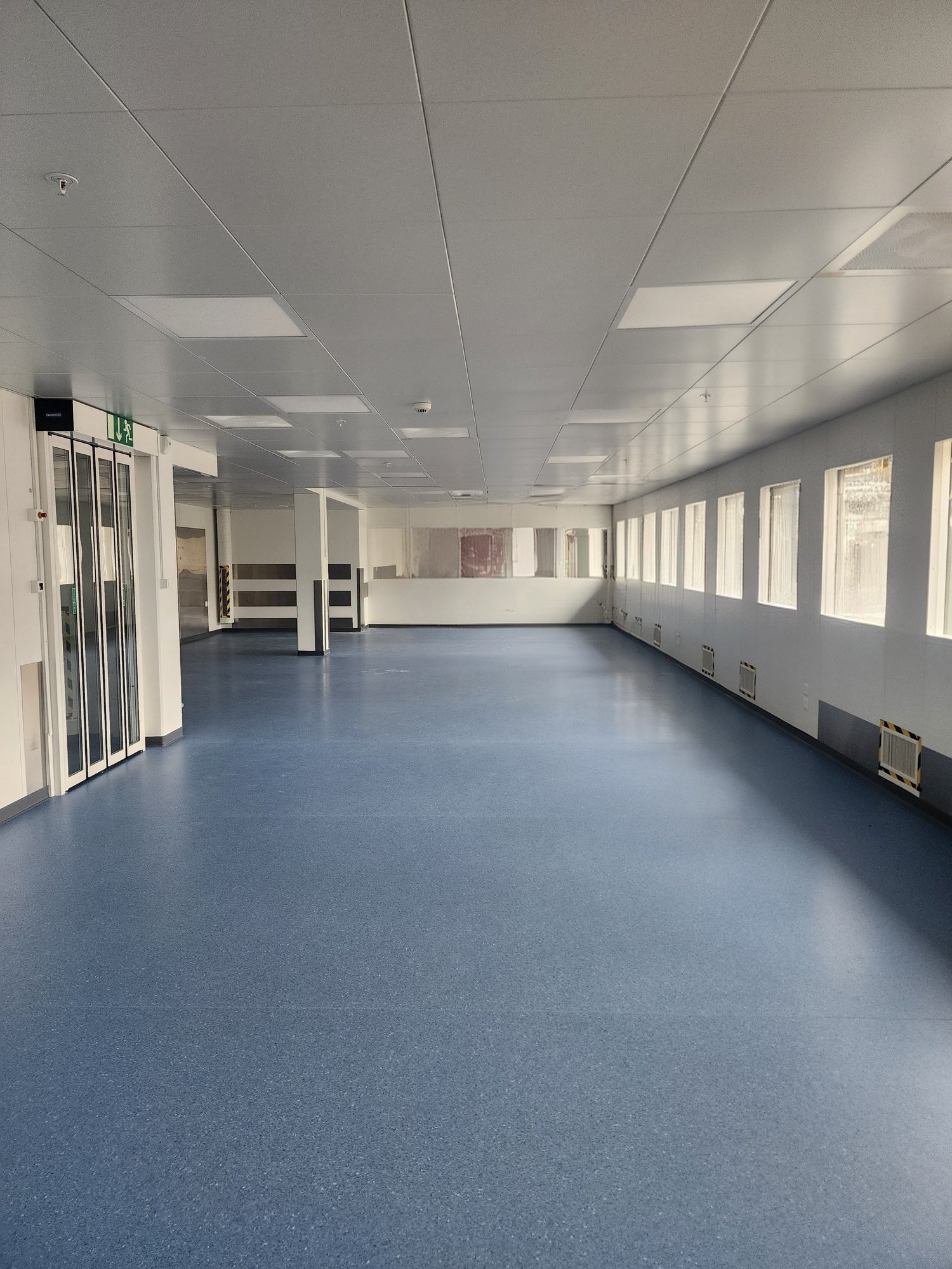 Empty room, white walls, blue floor, many windows, air vents on the walls