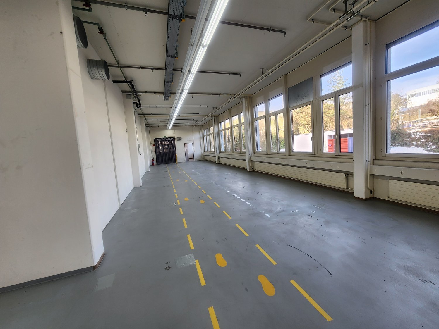 industrial warehouse, white walls, yellow painted lines on floor, tall windows, two doors on left