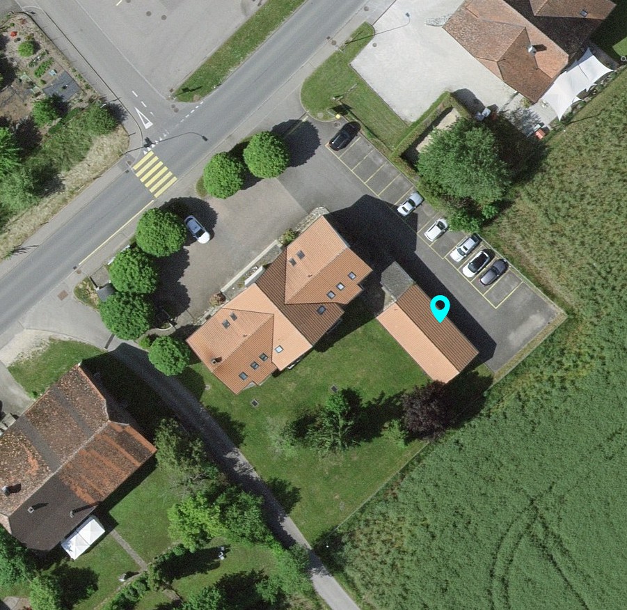 A two story house with brown roof, parking area with several cars parked, trees in the area