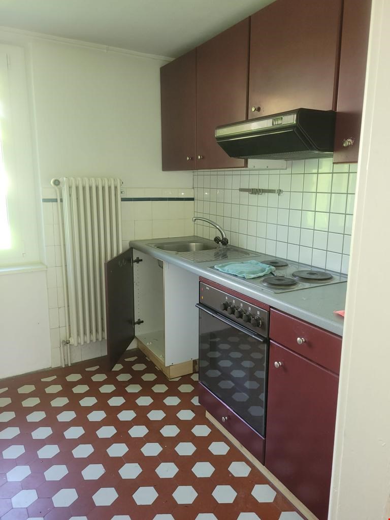 Compact kitchen with brown cabinets, white tile backsplash, stove, sink, and hexagonal tile flooring