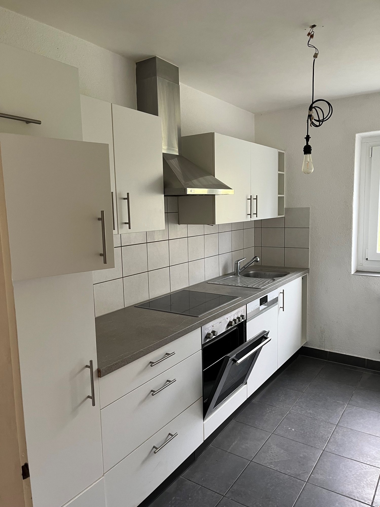 Modern kitchen with white cabinets, stainless steel appliances including a dishwasher, and gray tile flooring.