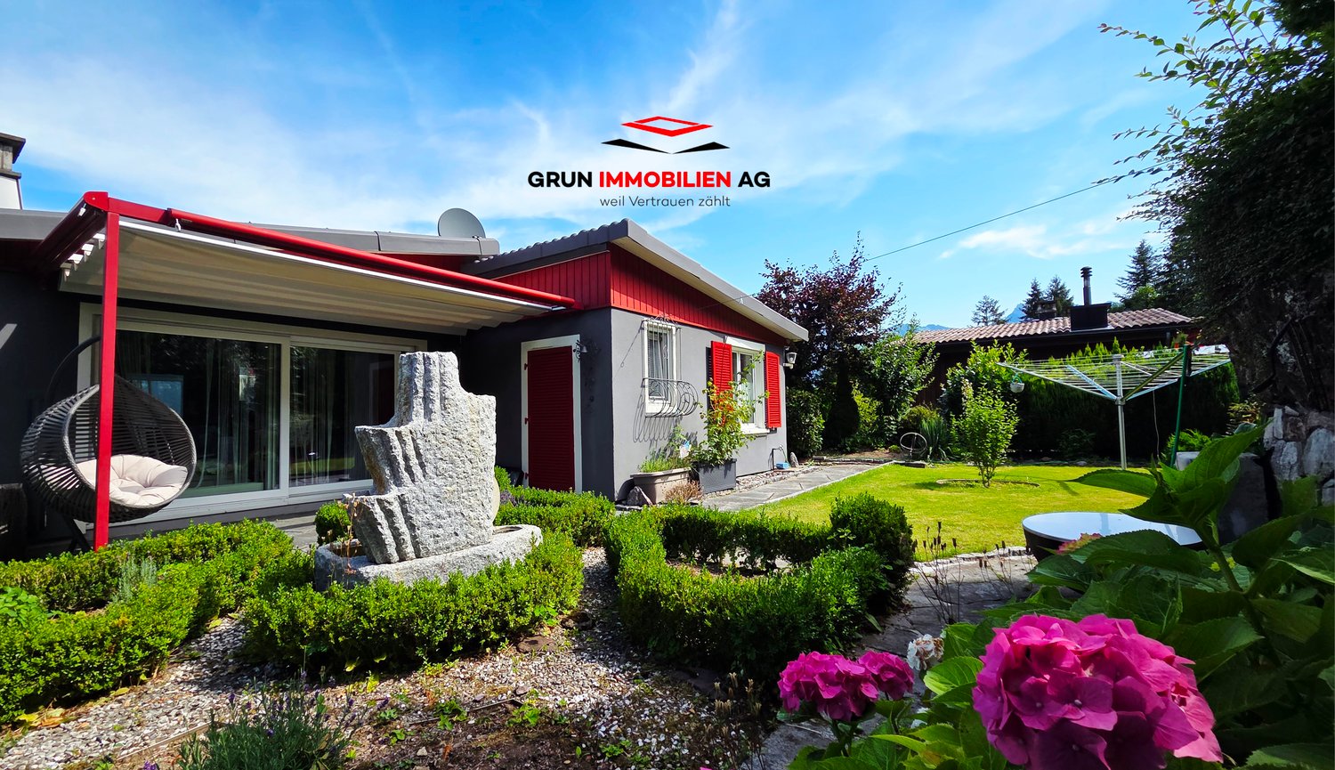 A gray and red house with a stone statue, glass windows, and a hanging chair