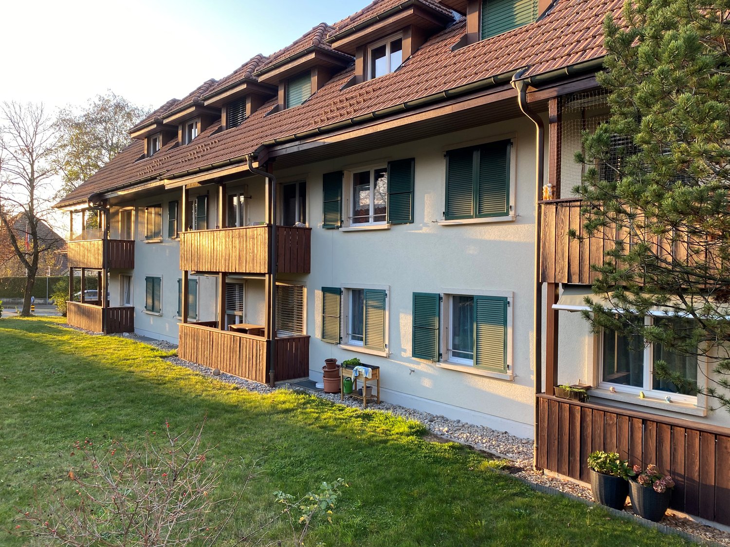 3 story apartment building, red roof, wooden balconies, white walls, green windows, grassy area