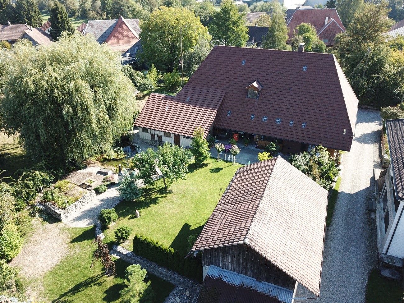 House: brown roof, white windows, garden, parking area, swimming pool, surrounded by greenery