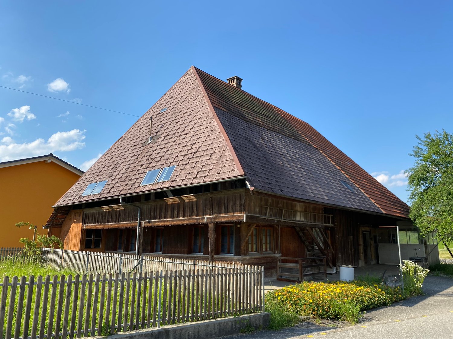 wooden traditional house, tiled roof, solar panels on roof, wooden fence, yellow flowers