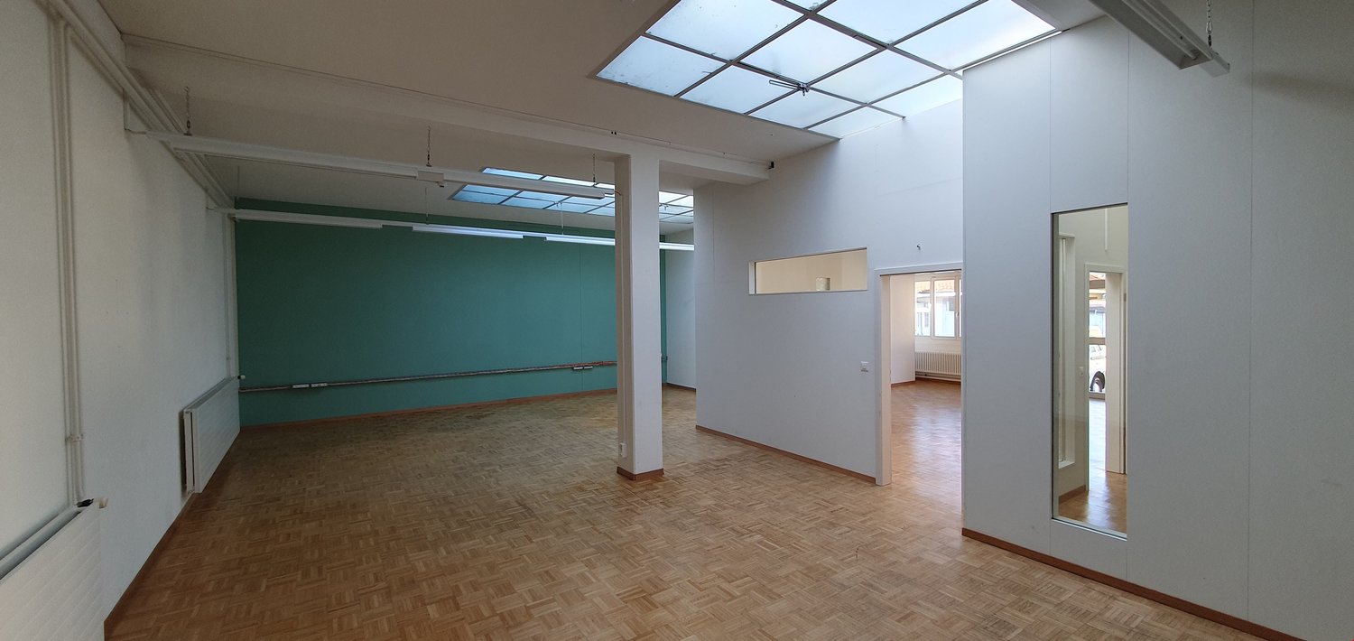 Empty room with wooden floor, white walls, glass windows, and ceiling lights