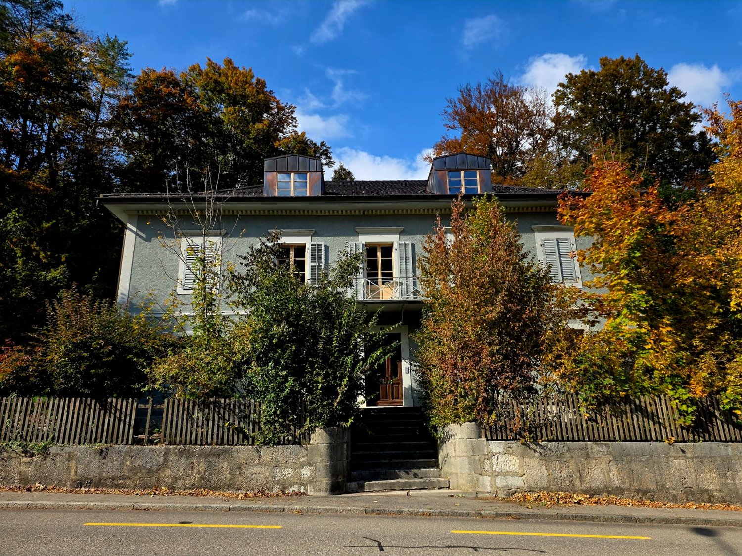 2 story house, gray exterior, brown door, balcony, staircase, fence, autumn trees