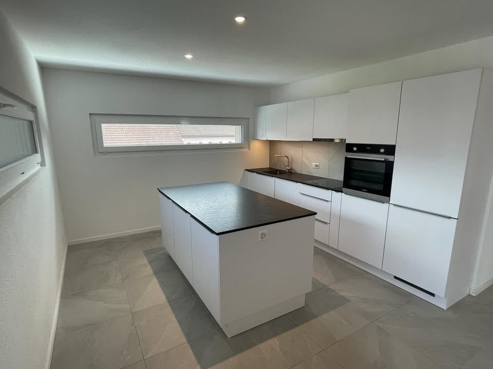 Fully equipped kitchen with white cabinets, black granite countertop, under-cabinet lighting, central island, integrated appliances, tiled floor, and window.
