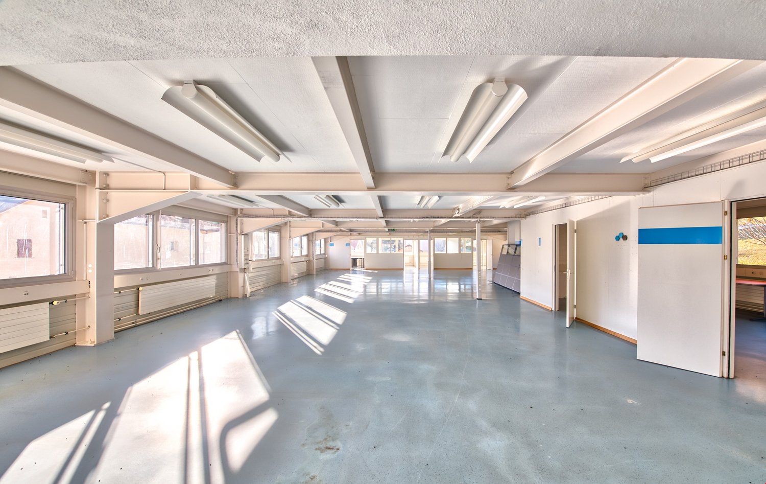 large open space, white walls and ceiling, windows, overhead lighting, radiators, clean