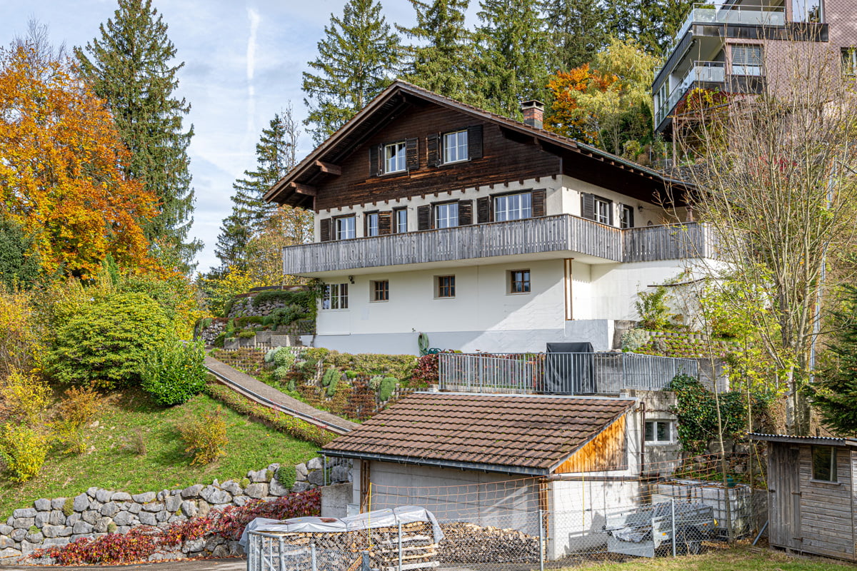 2-story house, brown roof, white walls, balcony, chimney, surrounded by trees and plants
