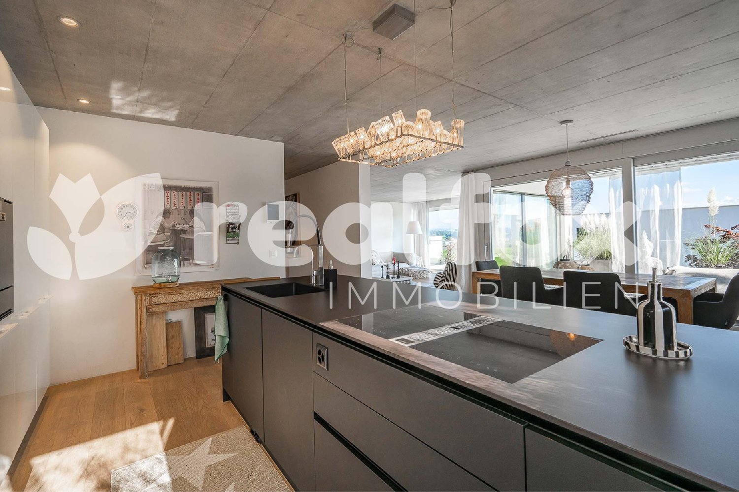 modern kitchen with large windows, wooden floor, large island with 2 sinks, chandelier, dining table, chairs