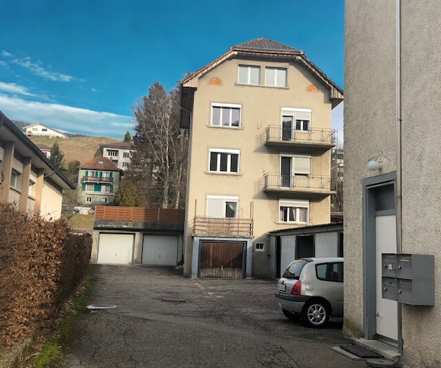 multi-story building, with 2 garages, a car parked in the driveway, hedges, brown grass