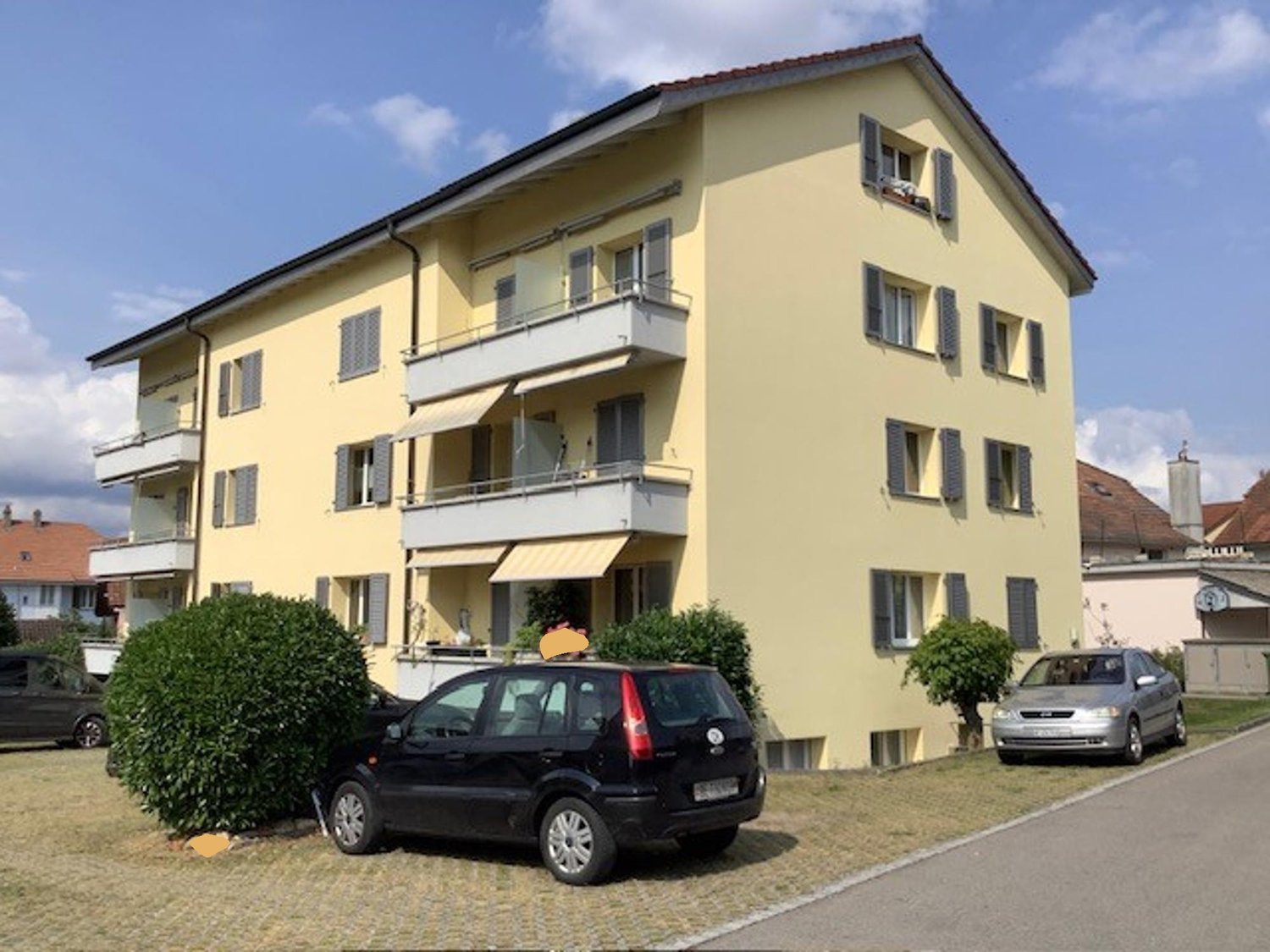 4 storey apartment building, yellow exterior, balconies on upper floors, parking area in front