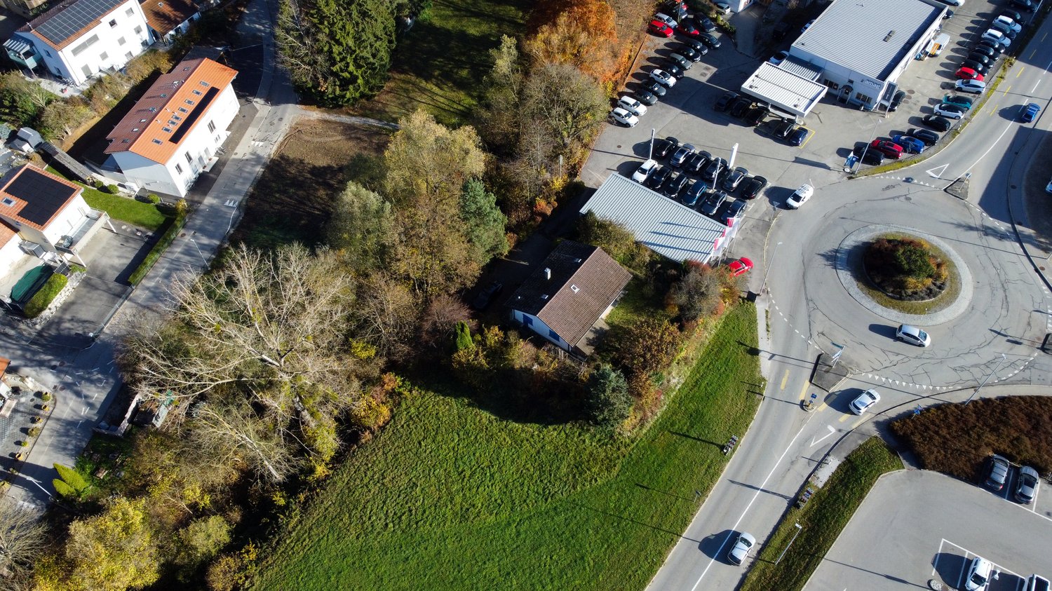 House, solar panels, multiple houses and commercial buildings in the area, grass and trees around, street with many cars parked and driving
