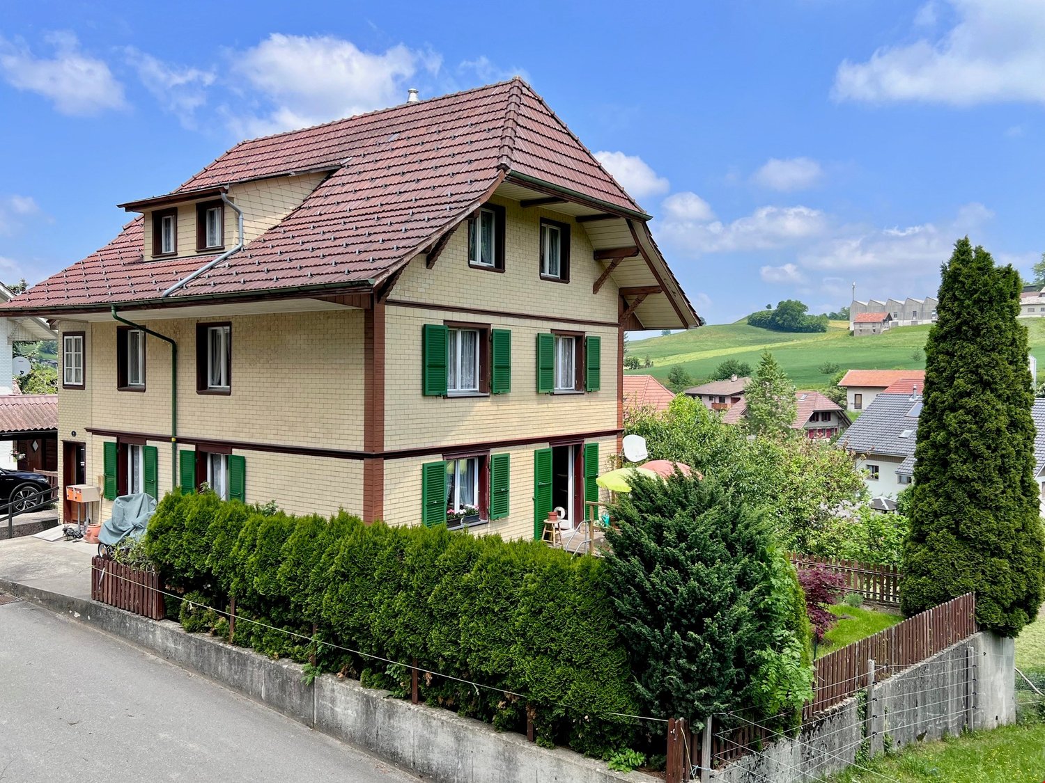 3 story house, red roof, beige walls, green shutters, black car in driveway