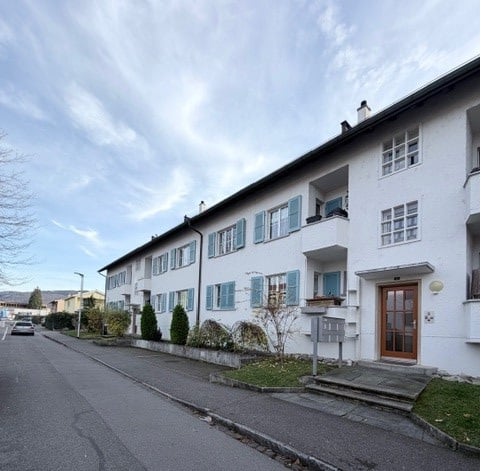 two story building, multiple apartments, white walls, blue shutters, small garden, sidewalk, street