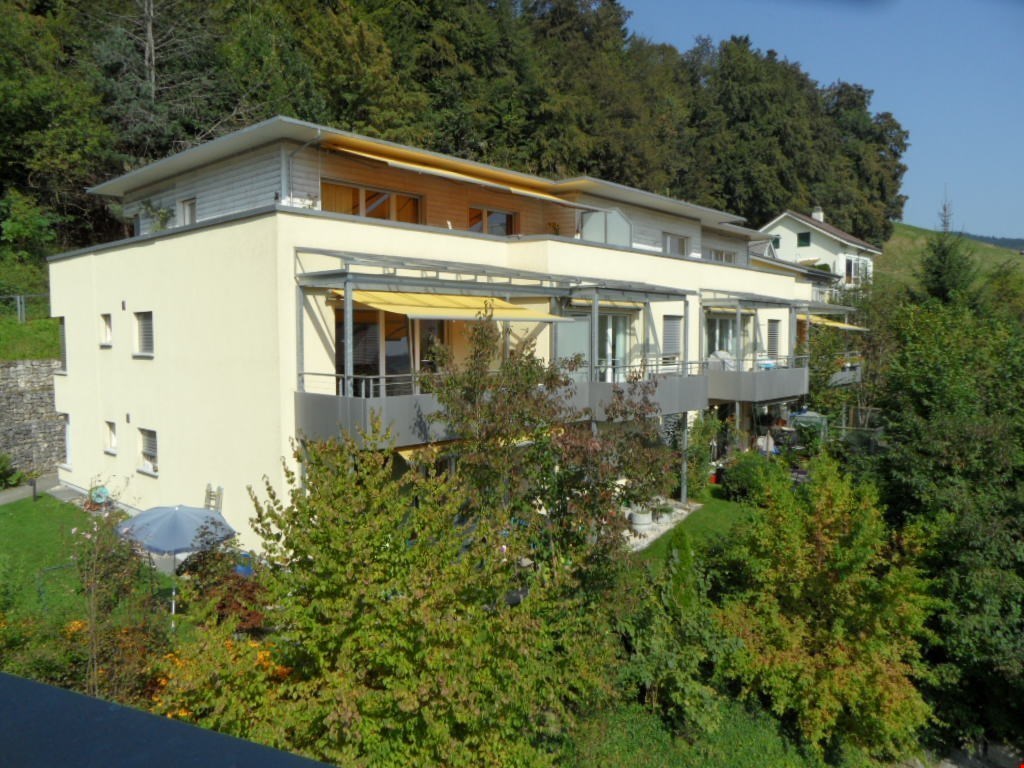 Two-story house, yellow exterior, sloped roof, balconies, surrounded by greenery