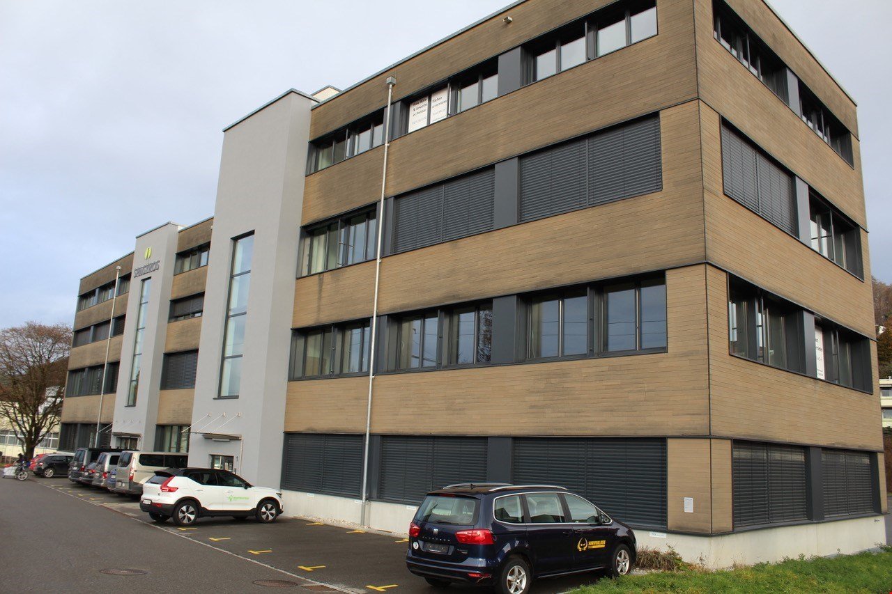 3 story modern office building, brown exterior, windows, parking area