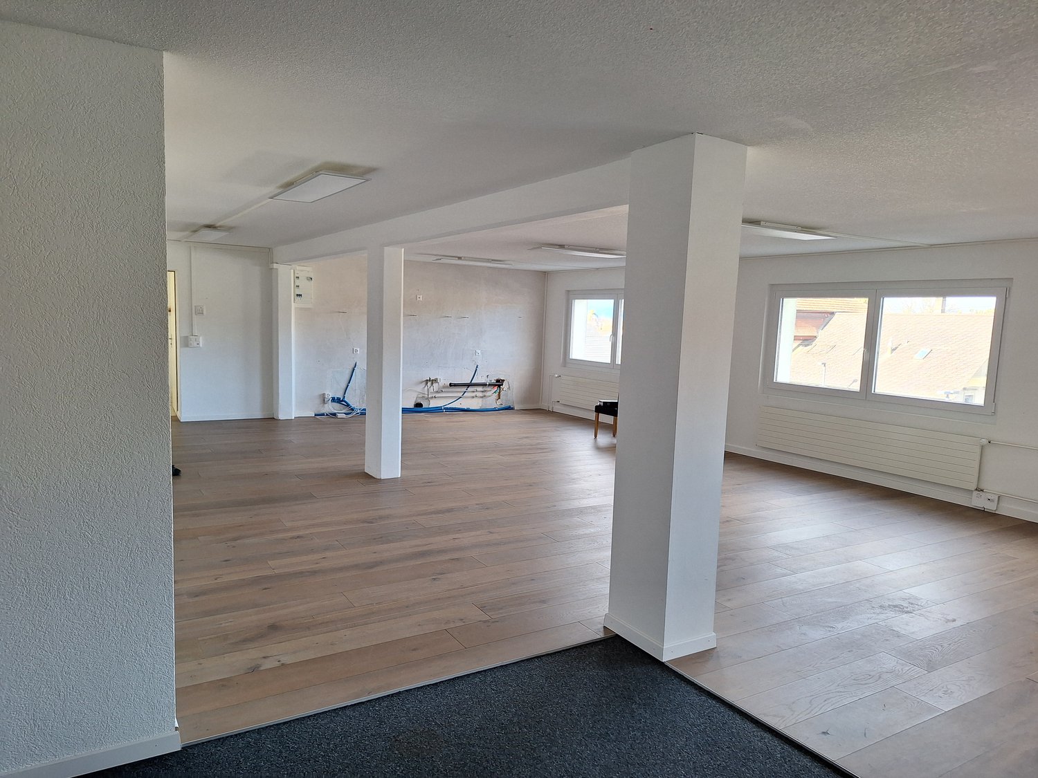 empty room, hardwood floor, white walls, 2 white pillars, 3 windows, radiator, ceiling lights