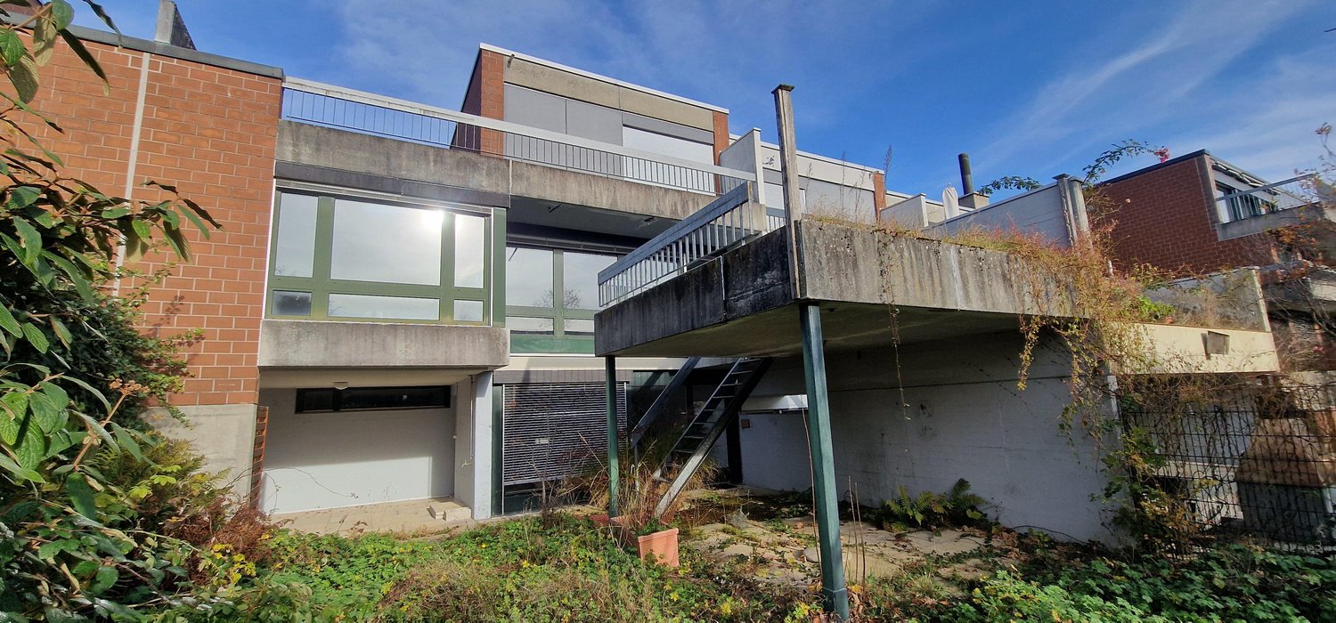 Two story house with brick and concrete design, terrace on the upper floor, and stairs leading to the lower floor.