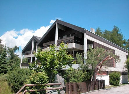 2-story modern house with a slanted roof, large balconies, and surrounded by trees and greenery.