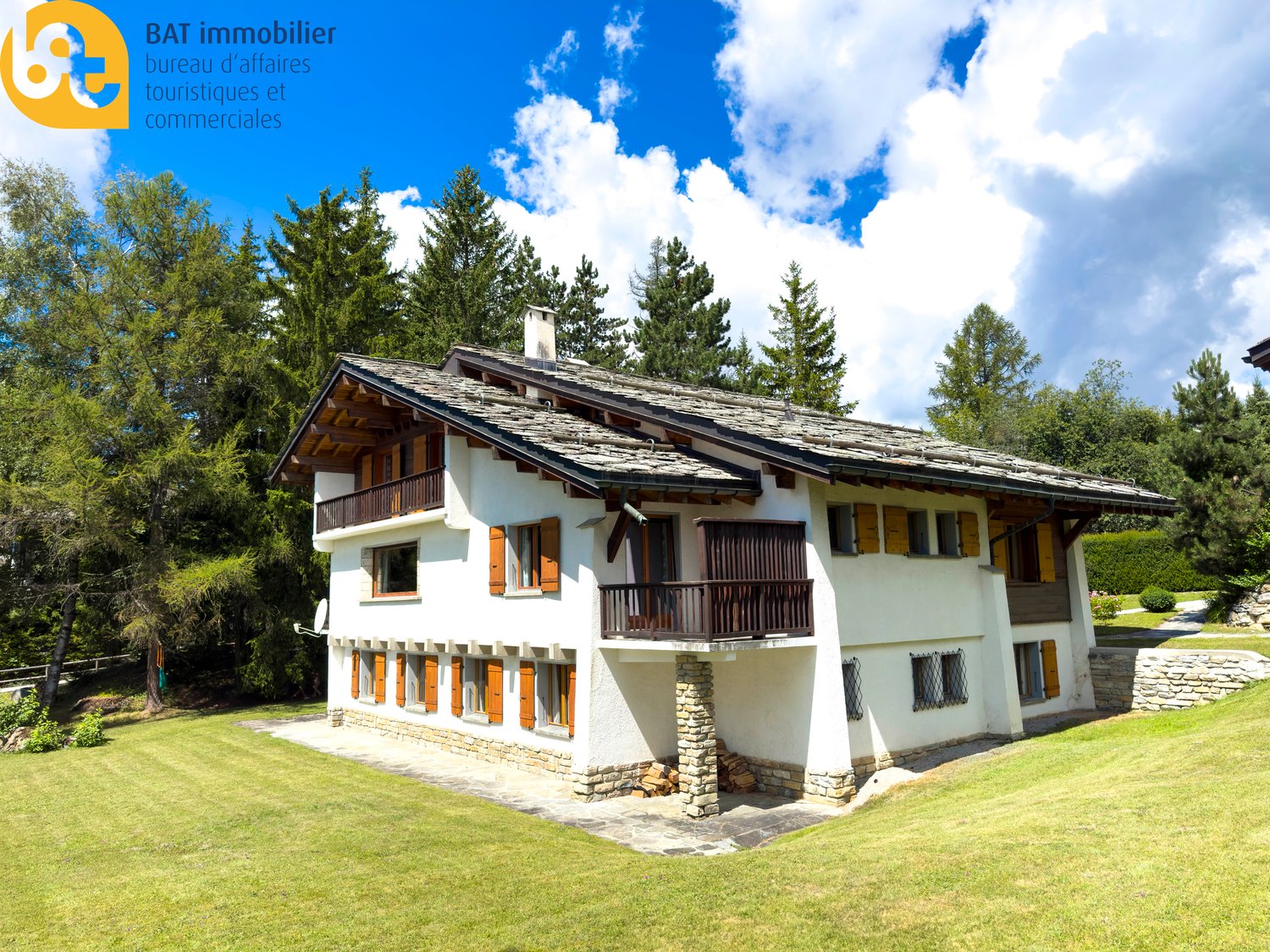 Alpine-style house, white exterior, wooden balcony, green roof, large windows, surrounded by a green lawn and trees