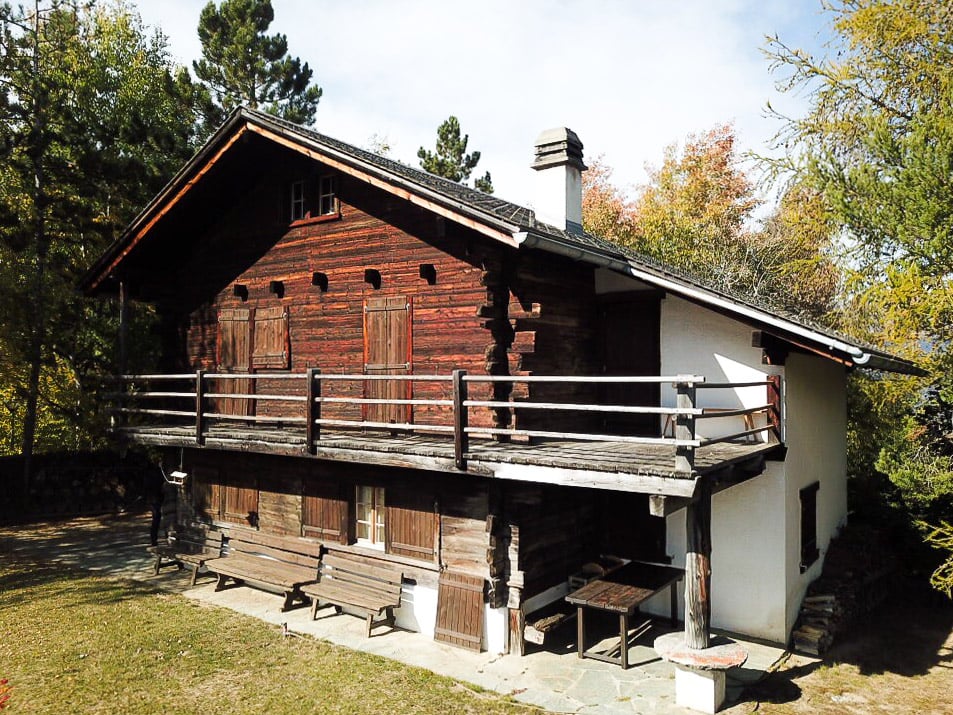 wooden chalet, wooden balcony, red brick, wooden doors, windows, outdoor table and benches, chimney