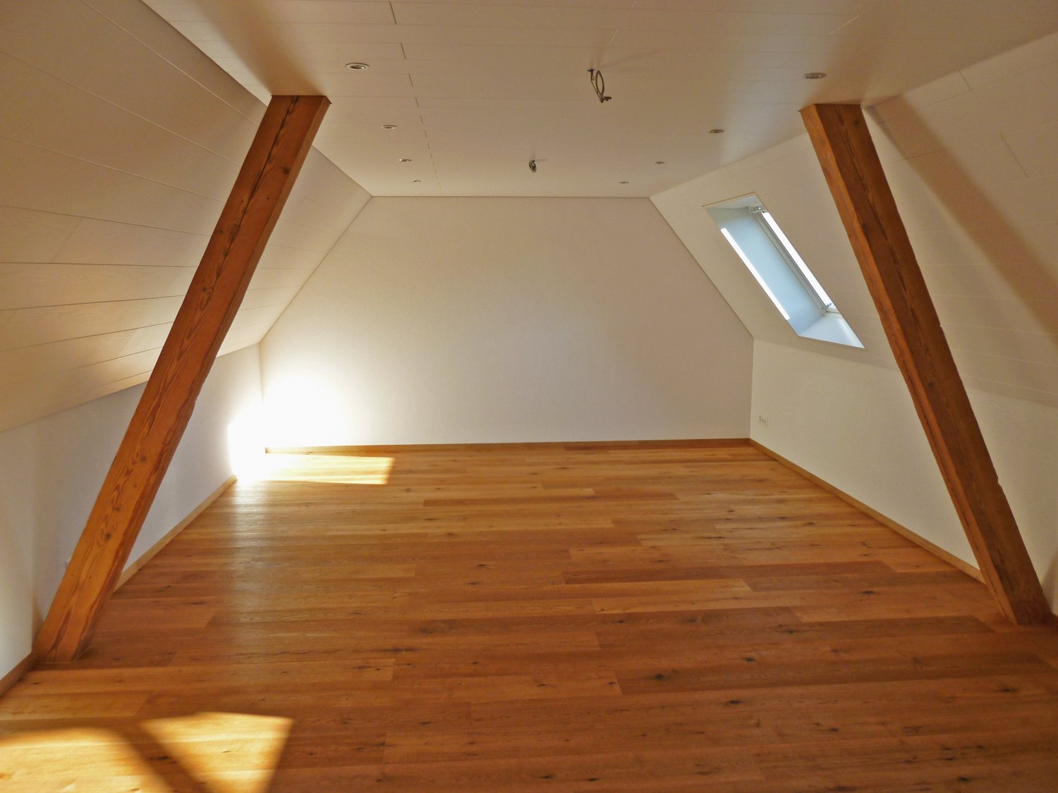Spacious attic room with wooden beams, hardwood flooring, and a skylight window providing natural light.